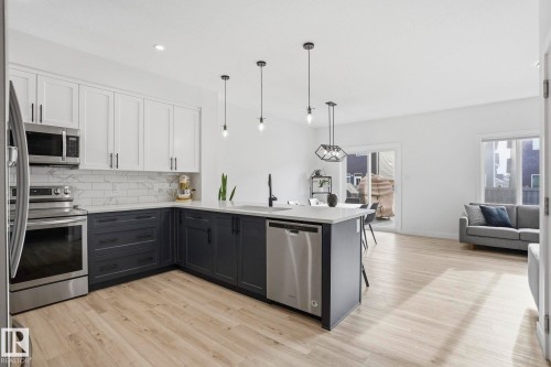 Kitchen with two tone cabinetry, stainless steel appliances, hanging light fixtures, decorative backsplash, and light wood-type flooring - 16627 31 Avenue, Edmonton, AB - Indoor Photo Showing Kitchen With Upgraded Kitchen
