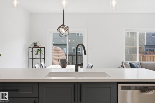 Kitchen with stainless steel dishwasher, hanging light fixtures, light stone counters, and gray cabinetry - 16627 31 Avenue, Edmonton, AB - Indoor Photo Showing Kitchen
