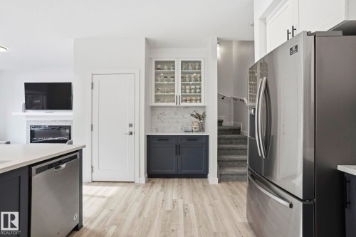 Two tone kitchen featuring stainless steel appliances, dual tone cabinets, glass fronted cabinets, light wood-type flooring, and a glass covered fireplace - 16627 31 Avenue, Edmonton, AB - Indoor Photo Showing Kitchen