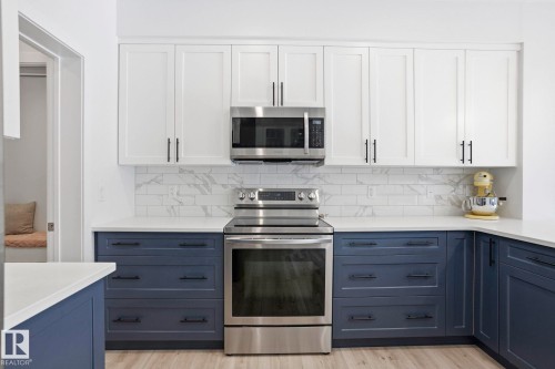 Kitchen featuring two tone cabinetry, stainless steel appliances, light stone counters, light wood-style flooring, and backsplash - 16627 31 Avenue, Edmonton, AB - Indoor Photo Showing Kitchen