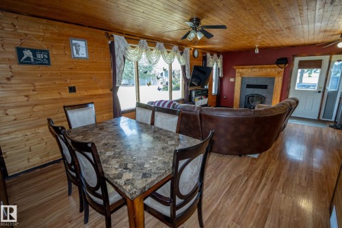 Dining area featuring a fireplace, a ceiling fan, wood finished floors, wood walls, and wooden ceiling - 56430 Range Rd 113, Rural St. Paul County, AB - Indoor Photo Showing Dining Room With Fireplace