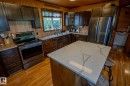 Kitchen featuring stainless steel appliances, wooden walls, a breakfast bar, a kitchen island, and light wood-type flooring - 56430 Range Rd 113, Rural St. Paul County, AB  - Indoor Photo Showing Kitchen With Double Sink 