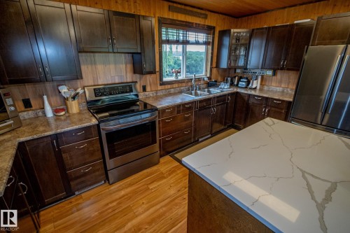 Kitchen featuring stainless steel appliances, dark wood finish cabinetry, light wood-style floors, wooden walls, and wood ceiling - 56430 Range Rd 113, Rural St. Paul County, AB - Indoor Photo Showing Kitchen With Double Sink