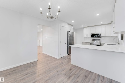 Kitchen featuring a peninsula, stainless steel appliances, white cabinetry, a chandelier, and light wood-style floors - 14511 21 St., Edmonton, AB - Indoor Photo Showing Kitchen With Upgraded Kitchen