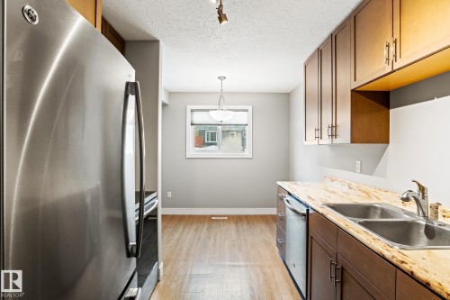 Kitchen featuring stainless steel appliances, light wood finished floors, decorative light fixtures, a textured ceiling, and light stone countertops - 914 9 Street, Cold Lake, AB - Indoor Photo Showing Kitchen With Double Sink