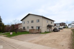 Two-story property with beige siding, a dark pitched roof, and multiple windows - 