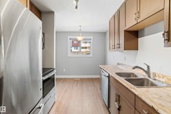 Kitchen with stainless steel appliances, light wood-style floors, a textured ceiling, wood finish cabinetry, and rail lighting - 