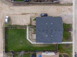 Aerial view showcasing a property with a dark shingle roof, a fenced grass yard, and a concrete pathway - 