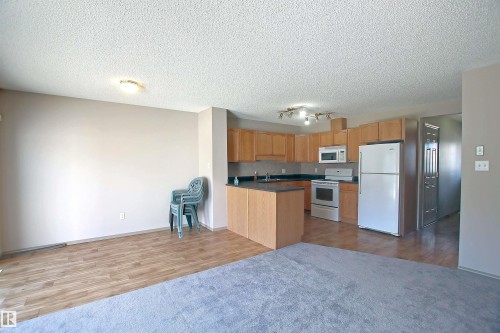 Kitchen featuring dark countertops, white appliances, dark wood finished floors, open floor plan, and a textured ceiling - 8129 7 Avenue, Edmonton, AB - Indoor Photo Showing Kitchen