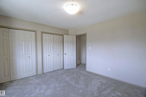 Unfurnished bedroom with two closets, a textured ceiling, and carpet floors - 8129 7 Avenue, Edmonton, AB - Indoor