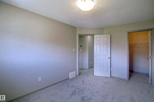 Unfurnished bedroom with carpet, a spacious closet, and a textured ceiling - 8129 7 Avenue, Edmonton, AB - Indoor Photo Showing Other Room