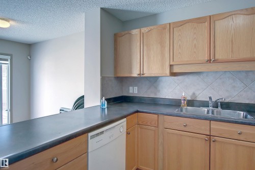 Kitchen with dishwasher, dark countertops, a textured ceiling, backsplash, and light brown cabinetry - 8129 7 Avenue, Edmonton, AB - Indoor Photo Showing Kitchen With Double Sink