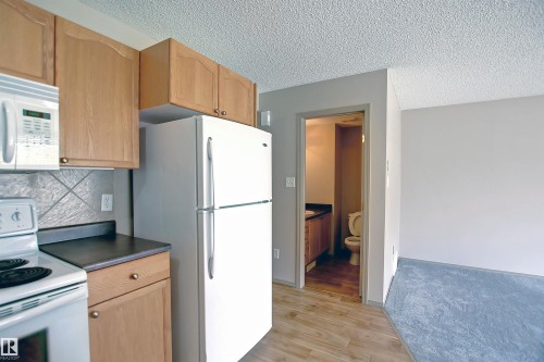 Kitchen featuring white appliances, dark countertops, a textured ceiling, light wood-style flooring, and backsplash - 8129 7 Avenue, Edmonton, AB - Indoor Photo Showing Kitchen