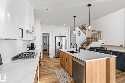 Two tone kitchen featuring two tone cabinets, open floor plan, stainless steel appliances, light wood finished floors, and hanging light fixtures - 342 Meadowview Drive, Fort Saskatchewan, AB - Indoor Photo Showing Kitchen With Double Sink With Upgraded Kitchen