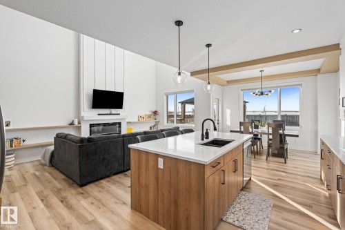Kitchen with open floor plan, a fireplace, light wood finished floors, wood finish cabinetry, and a raised ceiling - 342 Meadowview Drive, Fort Saskatchewan, AB - Indoor Photo Showing Kitchen