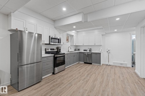 Kitchen featuring stainless steel appliances, dual tone cabinets, light countertops, a paneled ceiling, and light wood-style floors - 342 Meadowview Drive, Fort Saskatchewan, AB - Indoor Photo Showing Kitchen With Upgraded Kitchen
