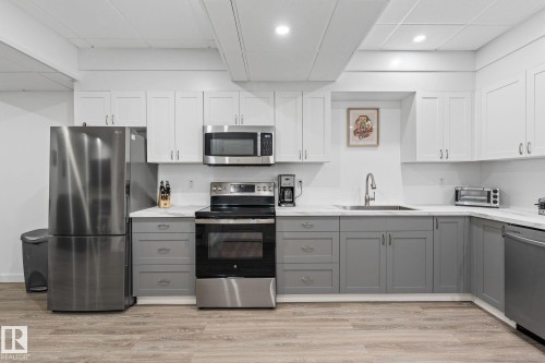Two tone kitchen featuring dual tone cabinets, stainless steel appliances, light wood-style floors, light stone counters, and a paneled ceiling - 342 Meadowview Drive, Fort Saskatchewan, AB - Indoor Photo Showing Kitchen