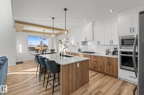 Kitchen with two tone cabinets, tasteful backsplash, light wood-type flooring, a center island with sink, and stainless steel appliances - 342 Meadowview Drive, Fort Saskatchewan, AB - Indoor Photo Showing Kitchen With Double Sink With Upgraded Kitchen