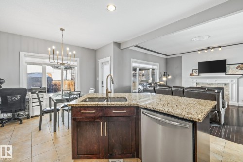 Kitchen with dishwasher, dark wood finish cabinetry, light stone countertops, open floor plan, and hanging lights - 167 Bremner Crescent, Fort Saskatchewan, AB - Indoor Photo Showing Kitchen With Double Sink With Upgraded Kitchen