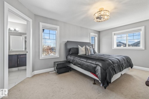 Bedroom with light colored carpet, ensuite bathroom, multiple windows, and suspended lighting - 167 Bremner Crescent, Fort Saskatchewan, AB - Indoor Photo Showing Bedroom