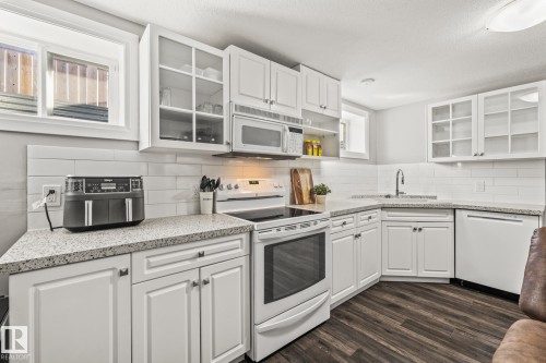 Kitchen featuring glass insert cabinets, white appliances, white cabinets, dark wood-style floors, and light stone counters - 167 Bremner Crescent, Fort Saskatchewan, AB - Indoor Photo Showing Kitchen
