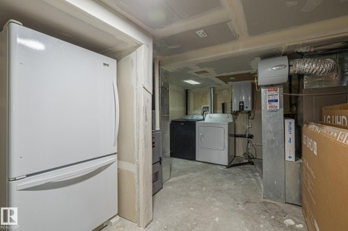 Unfinished below grade area with freestanding refrigerator, washing machine and clothes dryer, water heater, and heating unit - 167 Bremner Crescent, Fort Saskatchewan, AB - Indoor Photo Showing Laundry Room
