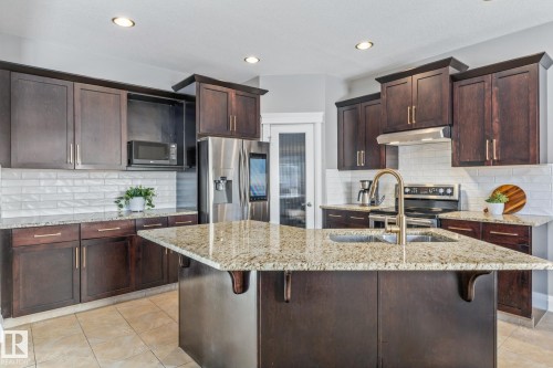 Kitchen featuring stainless steel appliances, a breakfast bar area, dark wood finish cabinets, light stone counters, and recessed lighting - 167 Bremner Crescent, Fort Saskatchewan, AB - Indoor Photo Showing Kitchen With Stainless Steel Kitchen With Double Sink With Upgraded Kitchen