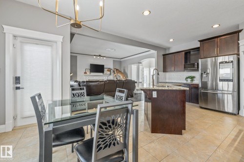 Kitchen featuring arched walkways, stainless steel refrigerator with ice dispenser, light stone countertops, dark wood finish cabinetry, and decorative backsplash - 167 Bremner Crescent, Fort Saskatchewan, AB - Indoor