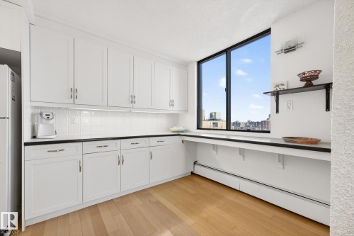 Kitchen with a baseboard radiator, light wood-style floors, white cabinetry, freestanding refrigerator, and decorative backsplash - 1502 10160 115 Street, Edmonton, AB - Indoor Photo Showing Kitchen
