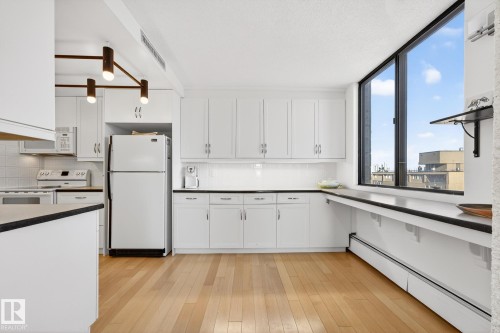Kitchen featuring a baseboard heating unit, white appliances, dark countertops, and white cabinets - 1502 10160 115 Street, Edmonton, AB - Indoor Photo Showing Kitchen