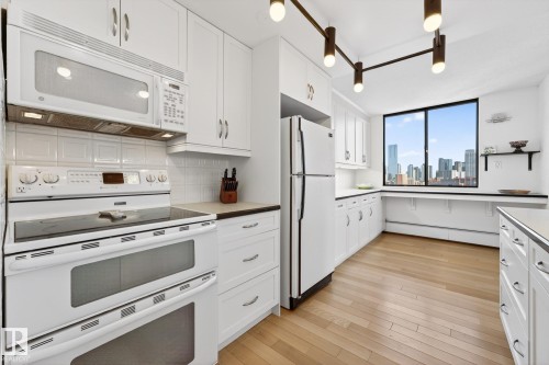 Kitchen with white appliances, white cabinets, a skyline view, light wood-style floors, and decorative backsplash - 1502 10160 115 Street, Edmonton, AB - Indoor Photo Showing Kitchen