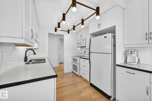Kitchen featuring backsplash, white appliances, white cabinetry, and light wood-type flooring - 1502 10160 115 Street, Edmonton, AB - Indoor Photo Showing Kitchen With Double Sink