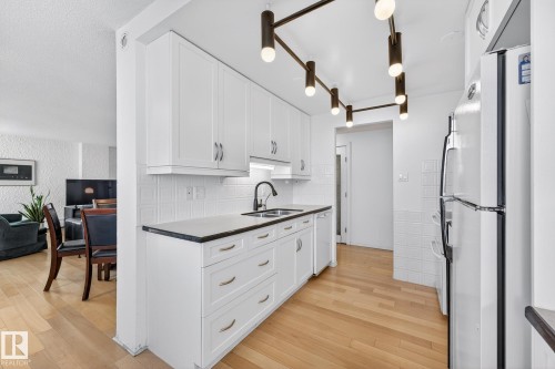 Kitchen featuring white cabinetry, white appliances, light wood-style floors, and backsplash - 1502 10160 115 Street, Edmonton, AB - Indoor Photo Showing Kitchen With Double Sink