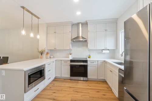 Kitchen with stainless steel appliances, decorative light fixtures, light wood-style flooring, backsplash, and a peninsula - 72 Penn Place, Spruce Grove, AB - Indoor Photo Showing Kitchen With Upgraded Kitchen