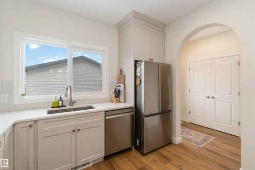 Kitchen featuring stainless steel appliances, arched walkways, light wood-style floors, light stone countertops, and white cabinetry - 72 Penn Place, Spruce Grove, AB - Indoor Photo Showing Kitchen