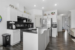 Kitchen featuring stainless steel appliances, dark wood-type flooring, decorative backsplash, and white cabinetry - 