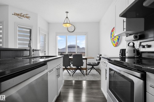 Kitchen featuring stainless steel appliances, white cabinets, range hood, and pendant lighting - 1965 118 Street, Edmonton, AB - Indoor Photo Showing Kitchen With Double Sink