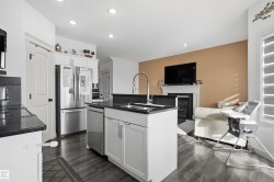 Kitchen featuring a glass covered fireplace, stainless steel appliances, white cabinetry, dark wood finished floors, and open floor plan - 