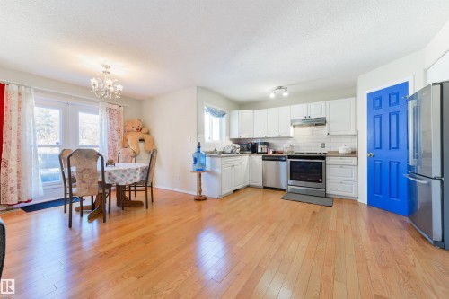 Kitchen featuring white cabinetry, stainless steel appliances, light wood-style flooring, hanging lights, and decorative backsplash - 11522 128 Street, Edmonton, AB - Indoor