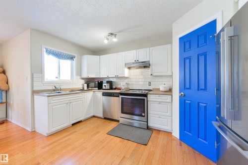 Kitchen featuring stainless steel appliances, white cabinetry, decorative backsplash, light wood-style flooring, and light countertops - 11522 128 Street, Edmonton, AB - Indoor Photo Showing Kitchen With Stainless Steel Kitchen