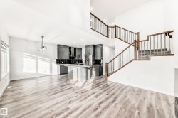 Unfurnished living room featuring a towering ceiling, light wood-style floors, recessed lighting, and stairway - 