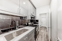 Kitchen with stainless steel gas range, decorative backsplash, under cabinet range hood, modern cabinets, and light wood-style flooring - 