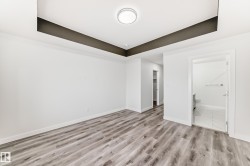 Unfurnished bedroom with a raised ceiling, light wood-style flooring, and ensuite bathroom - 