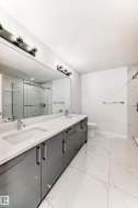 Bathroom with a marble finish shower, double vanity, a textured ceiling, and light marble finish flooring - 
