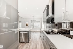 Kitchen featuring pendant lighting, stainless steel dishwasher, light wood-type flooring, wall chimney exhaust hood, and light stone countertops - 