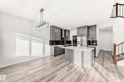 Kitchen with modern cabinets, gray cabinetry, a center island with sink, decorative light fixtures, and stainless steel fridge - 