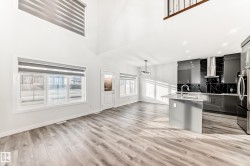 Kitchen with modern cabinets, an island with sink, a towering ceiling, gray cabinetry, and hanging light fixtures - 