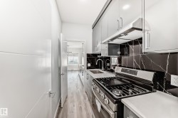 Kitchen featuring stainless steel range with gas stovetop, under cabinet range hood, light wood-type flooring, decorative backsplash, and light countertops - 