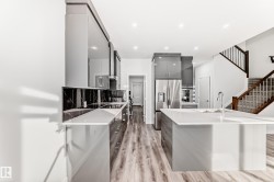 Kitchen with modern cabinets, stainless steel fridge, a kitchen island with sink, light wood-style floors, and gray cabinetry - 