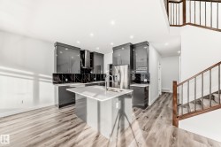 Kitchen featuring modern cabinets, gray cabinets, a center island with sink, stainless steel refrigerator with ice dispenser, and a breakfast bar area - 